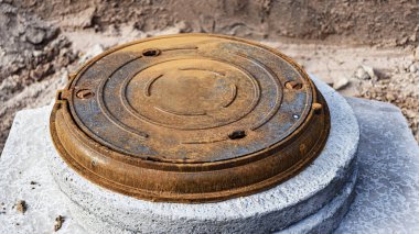 Beton bir kuyuya ağır demir kanalizasyon kapağı monte ediliyor. Yakın plan. Şehirde modern kanalizasyon ve su şebekesi