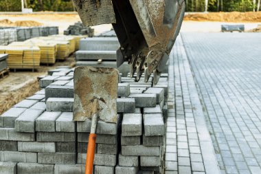 Mini bir kazıcı kovası bir inşaat alanındaki kaldırım levhalarının üzerinde duruyor. Toprak işleri ve peyzaj için komplike inşaat ekipmanları