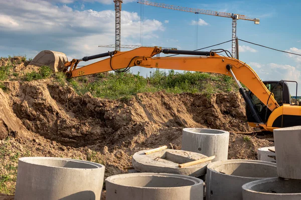 Bir kazıcı, bir konut inşaatı için bir temel kazıyor. Arka planda yeni binalar var. İnşaat üretimi. Kazı