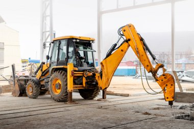 Endüstriyel hidrolik çekiçle ve kazıcıyla güçlendirilmiş beton yapıların profesyonel yıkımı. Üretim alanındaki beton zeminin sökülmesi. Enkaz ve beton kırıntıları.