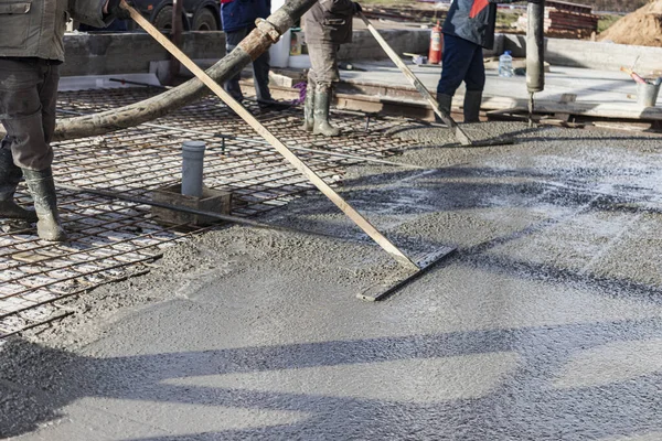 İnşaat işçisi endüstriyel bir atölyede beton döşemeyi yıkıyor. Bacakları betonun içinde. Yüzey somutlaşıyor. Monolitik güçlendirilmiş beton çalışmalar