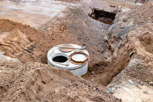 Монтаж железобетонной скважины для водоснабжения и канализации на строительной площадке. Кольца с чугунным люком и строительным инструментом