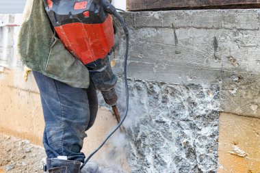 İnşaat alanında elinde kaya matkabı olan bir işçi beton duvarı yıkıyor. Güçlü manuel endüstriyel ekipman. İnşaat işi zor