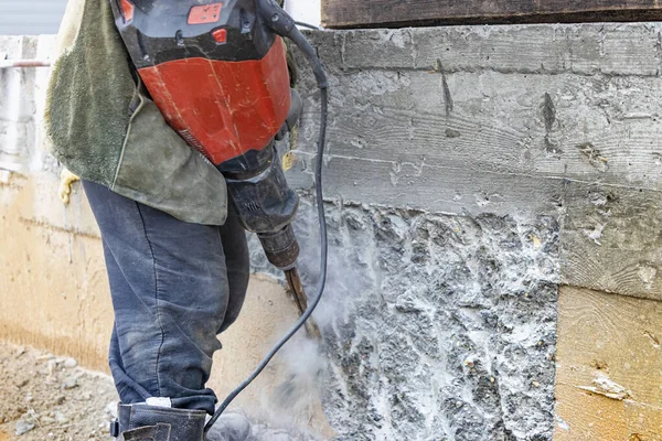 İnşaat alanında elinde kaya matkabı olan bir işçi beton duvarı yıkıyor. Güçlü manuel endüstriyel ekipman. İnşaat işi zor
