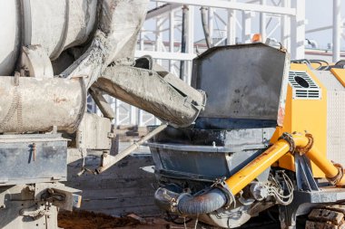 Beton karıştırıcı bir kamyon inşaat alanında beton bir pompaya havan topu döker. Monolitik güçlendirilmiş beton işlerinin üretimi için beton ve harç tedariği. Yakın plan.