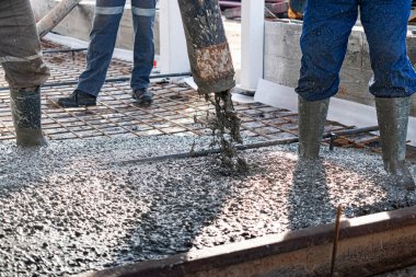 İnşaat işçileri sanayi atölyesinde beton döker. Bacakları betonun içinde. Döşeme için beton sunumu. Monolitik beton çalışmalar