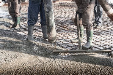 İnşaat işçileri sanayi atölyesinde beton döker. Bacakları betonun içinde. Döşeme için beton sunumu. Monolitik beton çalışmalar