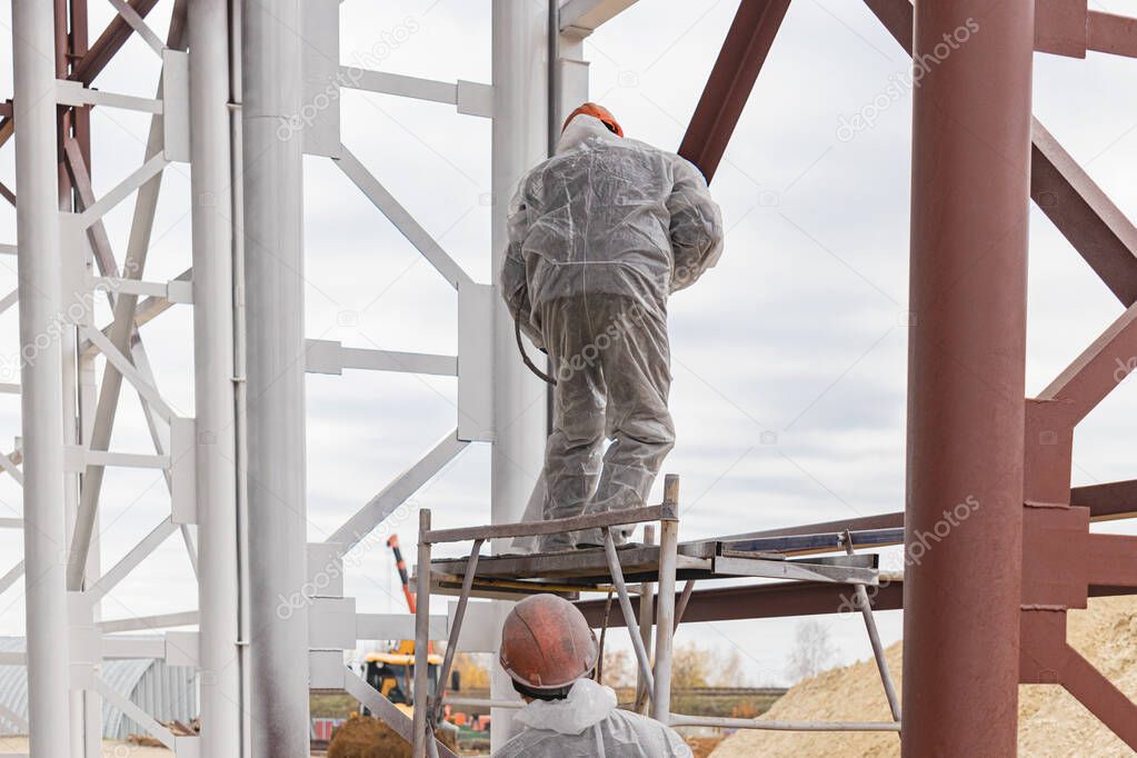 A worker in special protective clothing, works on painting and fire protection of metal structures at a height. Painting the metal at the construction site