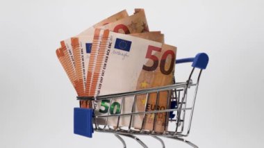 Bir marketten ya da beyaz bir arka planda hipermarketten bir sepetin içinde Euro banknotları. Yakın plan. İş ve finans. Para ve gıda harcamaları kavramı.