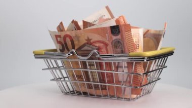 Bir marketten ya da beyaz bir arka planda hipermarketten bir sepetin içinde Euro banknotları. Yakın plan. İş ve finans. Para ve gıda harcamaları kavramı.