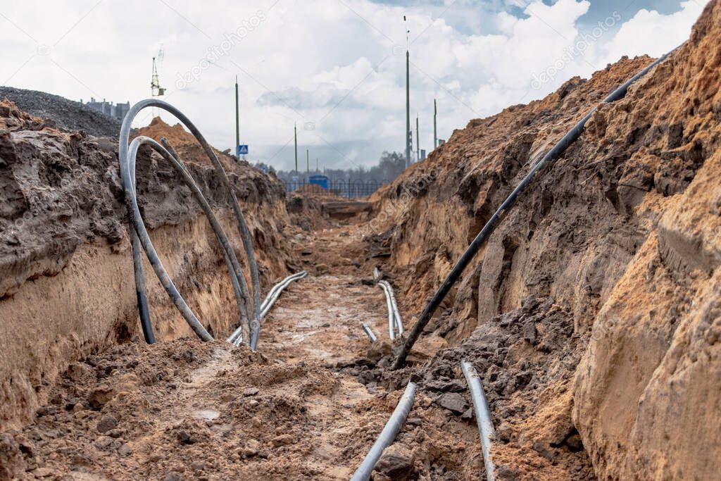 The high voltage electrical cable is laid in a trench under existing engineering sewerage networks. Laying a high voltage cable for supplying buildings with electricity