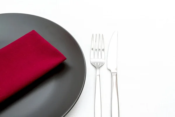 Черная тарелка со столовыми приборами и красной салфеткой — стоковое фото