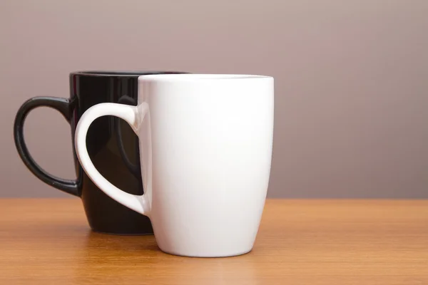 Zwart-wit koffiemokken op houten tafel — Stockfoto