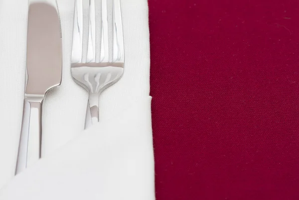 Talheres brilhantes em guardanapo branco dobrado na toalha de mesa vermelha — Fotografia de Stock