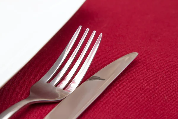 Cuchillo y tenedor con plato blanco sobre mantel rojo — Foto de Stock