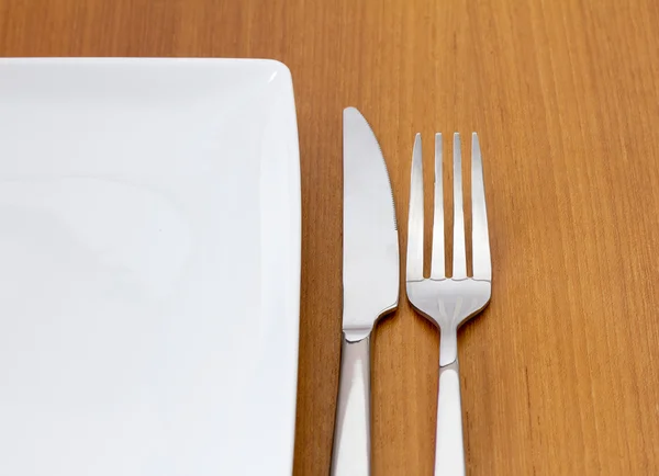 Knife and fork with white plate on wooden table — Stock Photo, Image
