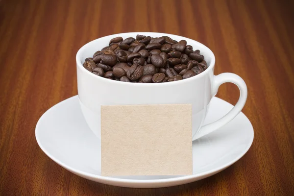 Taza de granos de café sobre mesa de madera con tarjeta para texto —  Fotos de Stock