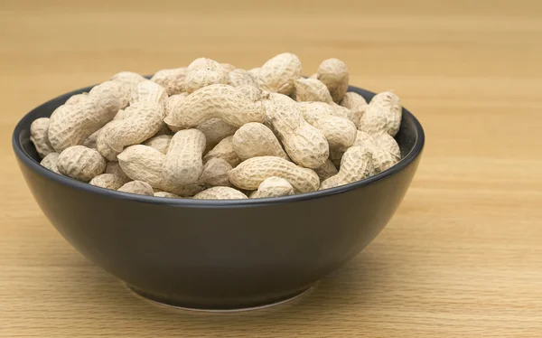 Peanuts in a black bowl on table — Stock Photo, Image