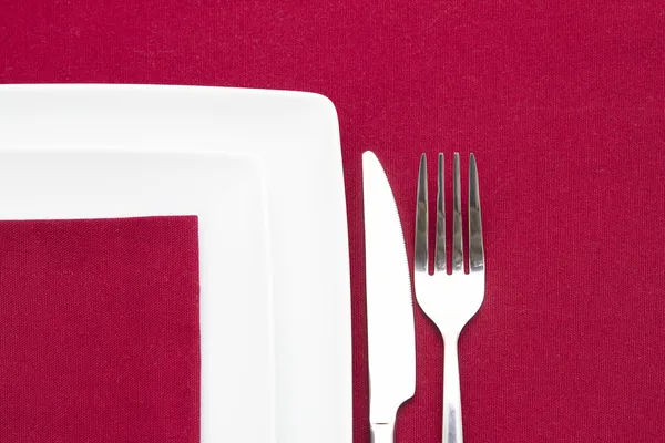 Two white square plates on red cloth with cutlery — Stock Photo, Image