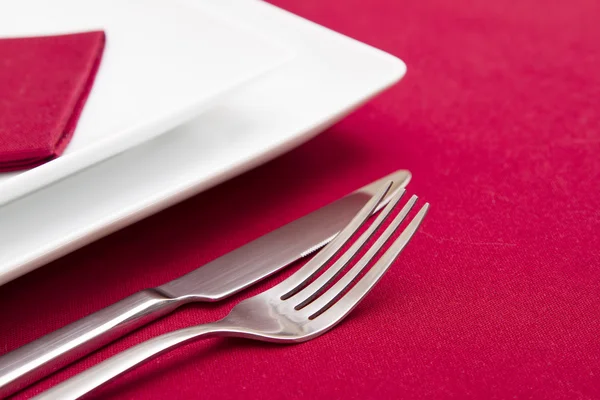 Нож и вилка с белыми пластинами на красной скатерти — стоковое фото