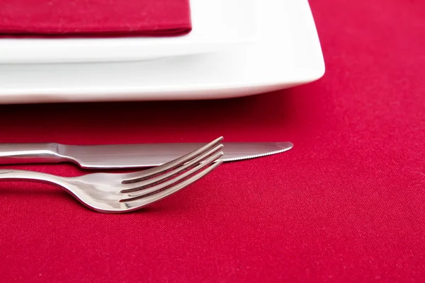 Cutlery and white square plates on red tablecloth — Stock Photo, Image