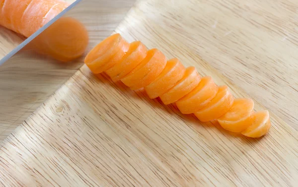 Carrot being sliced on wooden chopping board — Stock Photo, Image