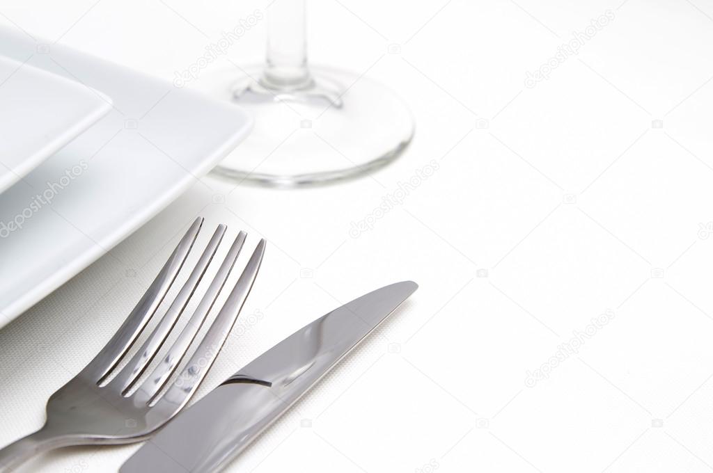 Dinner place setting. white square china plates with silver cutlery and glass