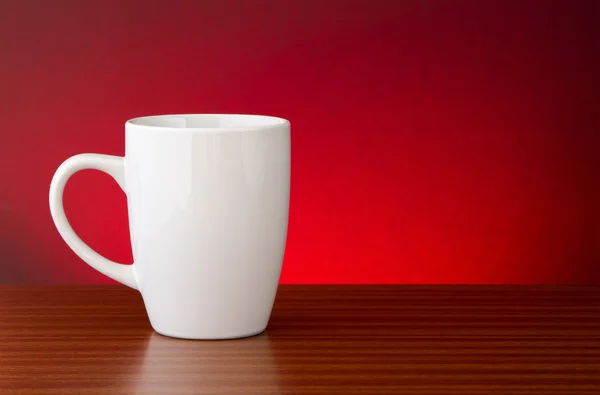 Taza blanca sobre mesa de madera oscura con fondo rojo brillante moteado —  Fotos de Stock