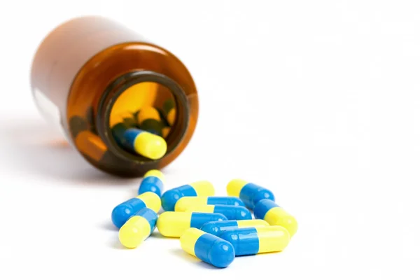 Yellow and blue pills with a brown bottle — Stock Photo, Image