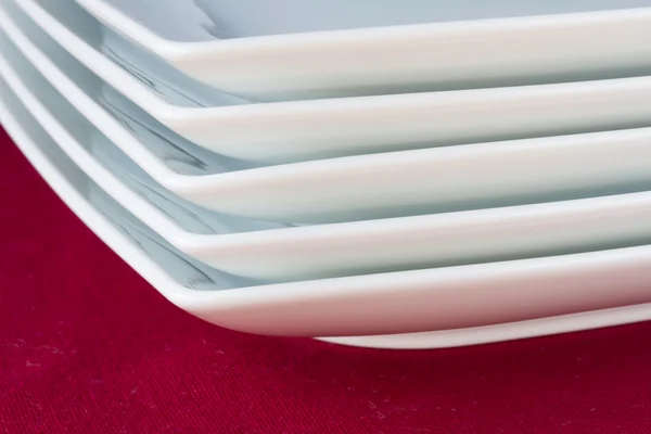 Kırmızı masa örtüsü üzerinde beyaz kare tabak yığını — Stok fotoğraf