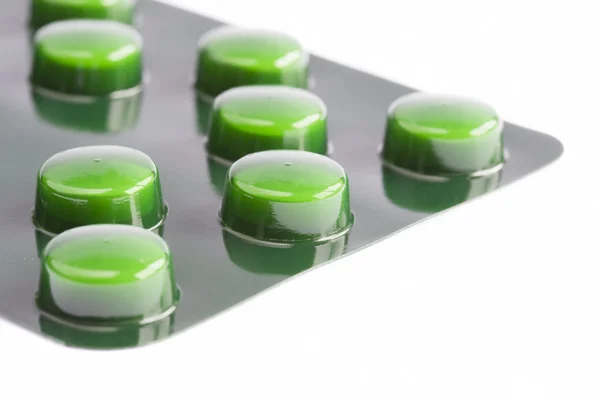 Зеленые таблетки в пузырьке на белом — стоковое фото