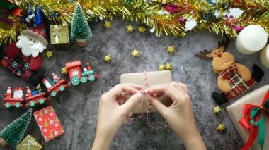 4 bin. Noel hediyesi olarak hediye paketi için kraft kağıdına sarılı bir ipe bir fiyonk bağlayan eller, Noel 'in kutlamaları sırasında süslemeli bir masaya, üst manzaraya. zanaat, boya ve el yapımı hediye
