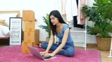 4 bin. Asyalı bir kadın bilgisayar defterine klavye yazıyor. Yatak odasının zemininde. Paket kutusuyla. E-ticaret, online alışveriş, çevrimiçi perakende mağazası, küçük işletme sahibi konsepti