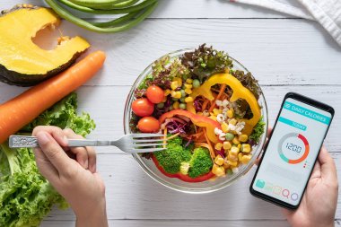 Kalori sayımı, diyet, gıda kontrolü ve kilo kaybı konsepti. Yemek masasındaki akıllı telefon ekranında salata, meyve suyu, ekmek ve taze sebzeyle kalori sayacı uygulaması. sağlıklı beslenme