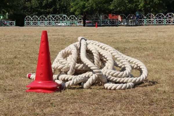 Kumaş ip, yeşil çimlerin üzerinde, spor sahasında izole edilmiş kırmızı bir koni ile uzanır.