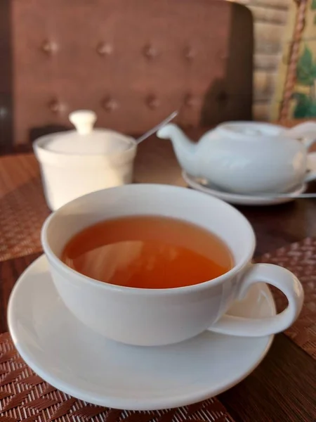 A large cup of tea on the table in front of the sugar bowl and teapot. Delicious black tea in a white cup