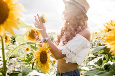 Manken görünümlü, sarışın, uzun saçlı, kot pantolonlu ve ayçiçeği tarlasında beyaz bluzu olan genç bir kız. Yüksek kalite fotoğraf
