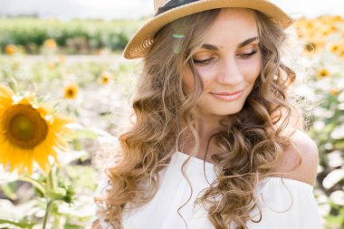 Manken görünümlü, sarışın, uzun saçlı, kot pantolonlu ve ayçiçeği tarlasında beyaz bluzu olan genç bir kız. Yüksek kalite fotoğraf