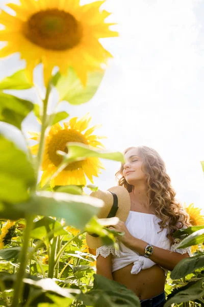 a young girl with a model appearance, blond and long hair, in denim trousers and a white blouse in a sunflower field. High quality photo