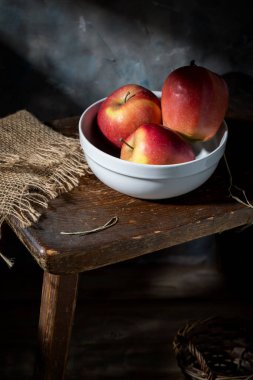 Beyaz bir fincanda kırmızı elmalar Eski bir bankta