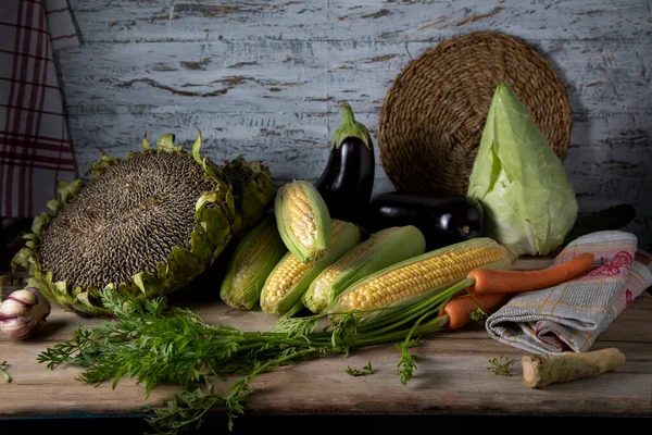 Fresh vegetables on a wooden table against a light wall. Carrots, eggplant, cabbage and corn