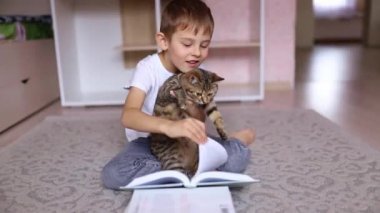 Kedisiyle kitap okuyan sevimli küçük bir çocuk. Evde eğitim. Mesafe öğrenme. Tatillerde. Coronavirüs salgını sırasında karantina. Kilitlenme