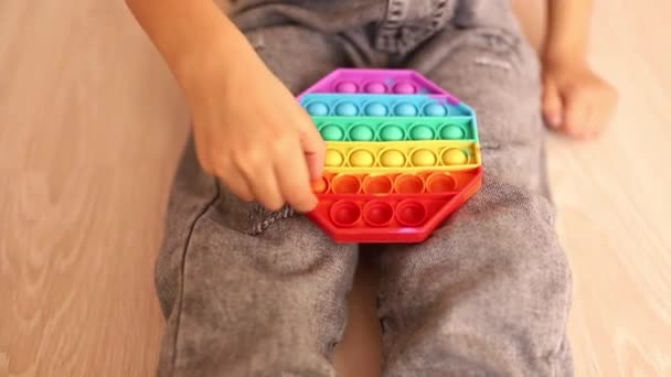 Ett barn med en färgglad pop det spel. Anti-stress. Populär Avslappnande romb form silikon stress leksak. Spel för barn under karantän och isolering — Stockvideo