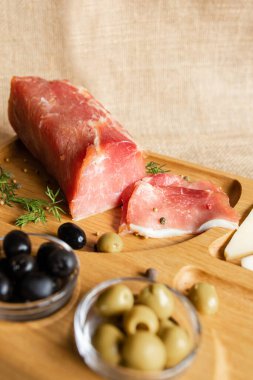 Tahtada kurutulmuş domuz filetosu peynir, zeytin, karabiber ve domates sosuyla servis ediliyor. Kurutulmuş fileto aperatifi. Beyaz Rusya mutfağı tabağı..