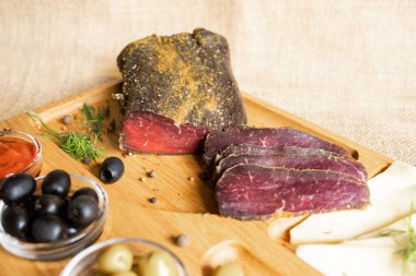 İnce dilimlenmiş sığır filetosu peynirli, zeytinli, karabiberli, domates soslu ahşap servis tahtasının üzerinde. Kurutulmuş fileto aperatifi. Beyaz Rusya mutfağı tabağı.