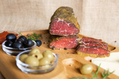 İnce dilimlenmiş sığır filetosu peynirli, zeytinli, karabiberli, domates soslu ahşap servis tahtasının üzerinde. Kurutulmuş fileto aperatifi. Beyaz Rusya mutfağı tabağı.