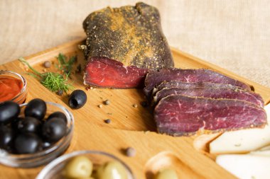 İnce dilimlenmiş sığır filetosu peynirli, zeytinli, karabiberli, domates soslu ahşap servis tahtasının üzerinde. Kurutulmuş fileto aperatifi. Beyaz Rusya mutfağı tabağı.