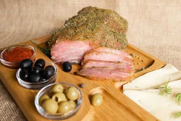 Tahtada kurutulmuş domuz filetosu peynir, zeytin, karabiber ve domates sosuyla servis ediliyor. Kurutulmuş fileto aperatifi. Belarus mutfağı tabağı. Yüksek kalite fotoğraf