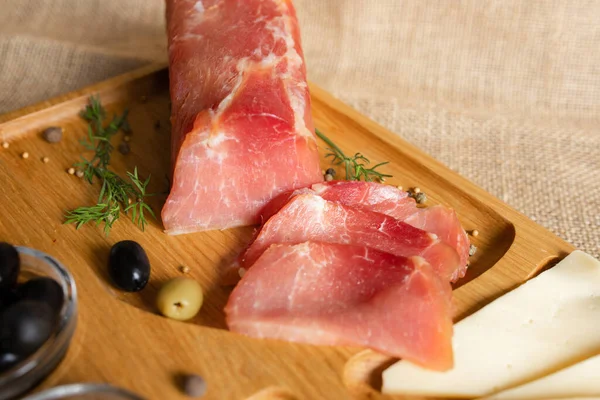 Tahtada kurutulmuş domuz filetosu peynir, zeytin, karabiber ve domates sosuyla servis ediliyor. Kurutulmuş fileto aperatifi. Belarus mutfağı tabağı. Yüksek kalite fotoğraf