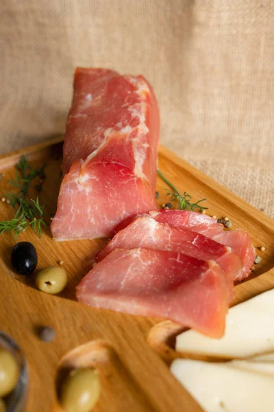 Tahtada kurutulmuş domuz filetosu peynir, zeytin, karabiber ve domates sosuyla servis ediliyor. Kurutulmuş fileto aperatifi. Belarus mutfağı tabağı. Yüksek kalite fotoğraf